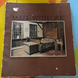 May include: A book titled "Made With Oak" by Jeffrey Friedman-Weiss and Herbert H Wise. The cover features a photograph of a bedroom with a wooden bed, a wicker basket, and a wooden barrel.