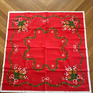 May include: Red tablecloth with a white border and a floral pattern of orange tulips and white lily of the valley flowers. The flowers are arranged in bouquets and are surrounded by a green garland.