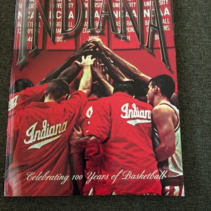 May include: A red book cover with the word "Indiana" in large letters. The cover features a photo of a basketball team huddle and the text "Celebrating 100 Years of Basketball."