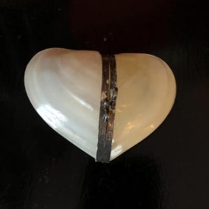 May include: A heart-shaped box made of white mother of pearl with a silver hinge and clasp.