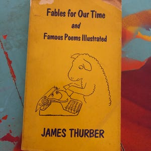 May include: A vintage book titled "Fables for Our Time and Famous Poems Illustrated" by James Thurber. The cover is yellow with black text and a cartoon illustration of a sheep typing on a typewriter. The book shows signs of wear.