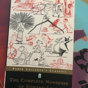 May include: A paperback book titled The Complete Nonsense of Edward Lear, edited by Holbrook Jackson, featuring a white cover with black and red whimsical line drawings of various characters, animals, and objects, published by Faber Children's Classics.