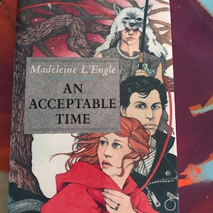 May include: A paperback book titled An Acceptable Time by Madeleine L'Engle. The cover features an illustration of a person with red hair in a red hooded garment, a person with dark hair, and a figure wearing a wolf headpiece against a tree.