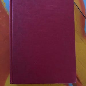 May include: A deep red hardcover book with a smooth, textured cover.