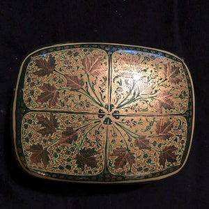 May include: Rectangular decorative box with a gold, green, and brown leaf design. The box has a dark green border and a gold interior. The leaf pattern is symmetrical, with four sections of leaves radiating from the center.