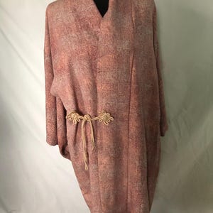 May include: A long, pink robe with a subtle pattern and a tie belt with decorative knots. The robe has a V-neck and long sleeves.