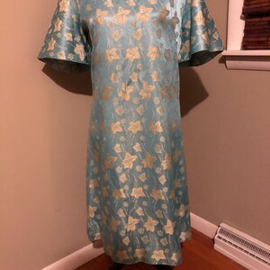 May include: A light blue dress with a gold floral pattern. The dress has short, flared sleeves and a scoop neckline. The dress is displayed on a black dress form.