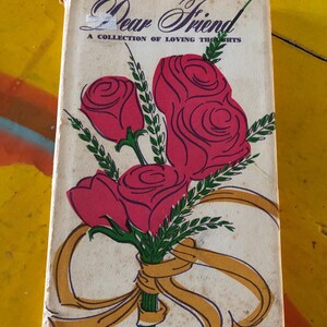 May include: Vintage book cover with the title "Dear Friend" and the subtitle "A Collection of Loving Thoughts." The cover features a bouquet of red roses tied with a gold ribbon. The background is off-white.
