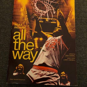May include: A vintage book cover featuring a basketball player in a red and white jersey, jumping to dunk a basketball. The cover has the text "NCAA Indiana all the way" and the book title is "All the Way".
