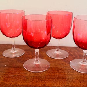 Puede incluir: Conjunto de seis copas de vino teñidas de rojo con tallos y bases transparentes. Las copas están dispuestas sobre una superficie de madera, mostrando su color vibrante y diseño elegante. Adecuado para servir vino u otras bebidas.