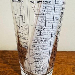 May include: Clear cocktail shaker glass with black text and illustrations for Manhattan and Whisky Sour cocktails. Includes measurements in milliliters and instructions. Features a classic design for home bars.