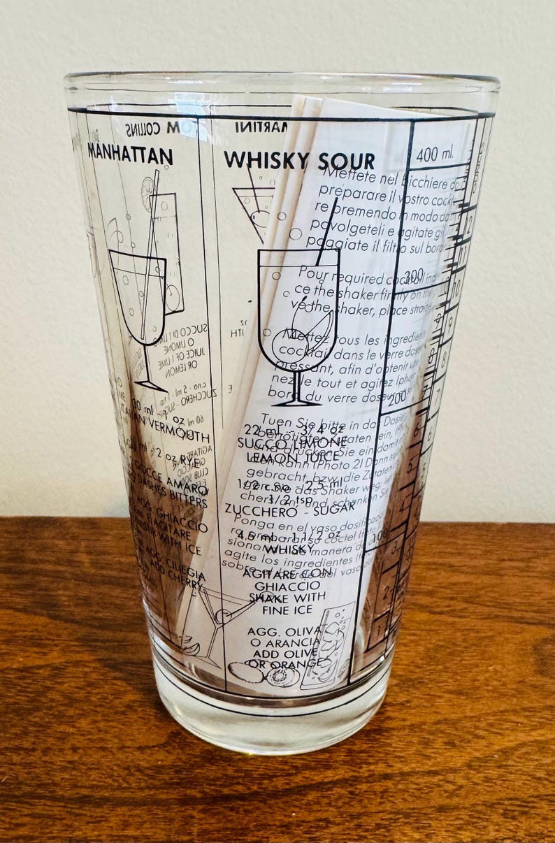 May include: Clear cocktail shaker glass with black text and illustrations for Manhattan and Whisky Sour cocktails. Includes measurements in milliliters and instructions. Features a classic design for home bars.