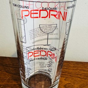 May include: Clear glass cocktail shaker with a flared shape. The shaker features a red and black design with the name "PEDRINI" and cocktail recipes. The text includes measurements in ounces and teaspoons.