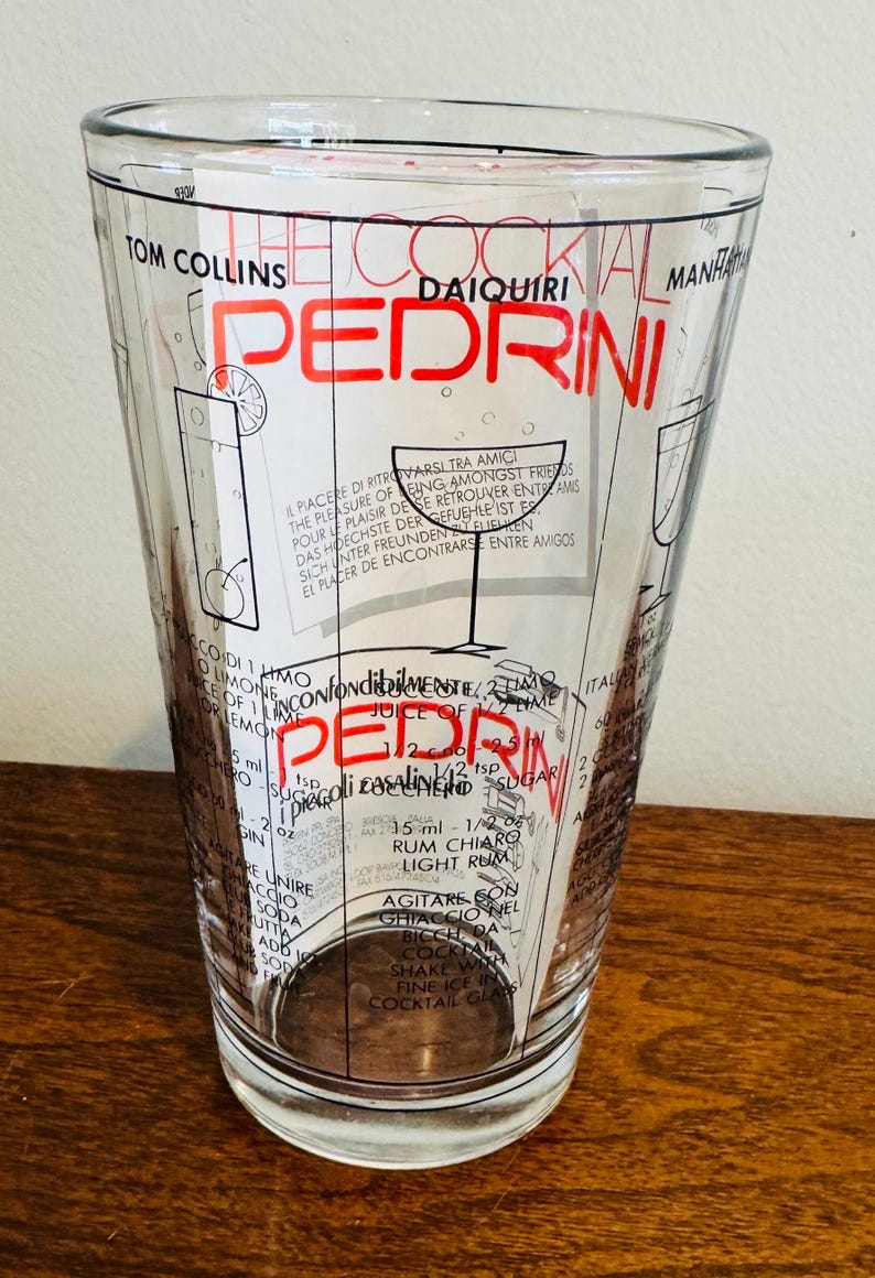 May include: Clear glass cocktail shaker with a flared shape. The shaker features a red and black design with the name "PEDRINI" and cocktail recipes. The text includes measurements in ounces and teaspoons.