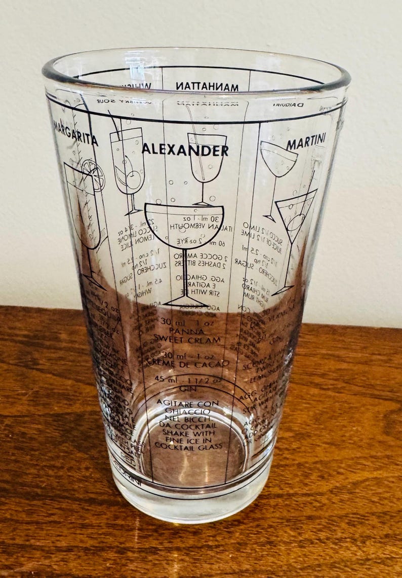 May include: Clear glass cocktail shaker with black printed cocktail recipes, including Margarita, Alexander, and Martini. The shaker has measurement markings in milliliters and ounces, and instructions for shaking with ice.