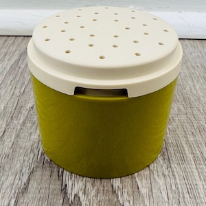 Könnte beinhalten: Ein vintage Behälter in Olivgrün und Creme mit einem perforierten Deckel. Der zylindrische Behälter hat eine strukturierte Oberfläche und einen cremefarbenen Deckel mit mehreren kleinen Löchern. Der Behälter ist wahrscheinlich für die Küche oder Speisekammer bestimmt.