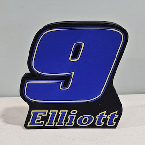 May include: A black, free-standing number nine with a blue background and yellow trim. The word "Elliott" is displayed in yellow at the base of the number. The number nine is a prominent feature of this item.