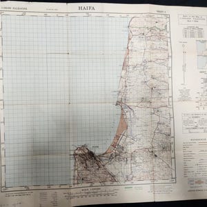 Puede incluir: Un mapa antiguo de Haifa, Palestina, con detalles geográficos, incluyendo costas, carreteras y áreas urbanas. El mapa está plegado y muestra un patrón de cuadrícula, con texto que indica la escala e información de referencia. Impreso en papel envejecido.
