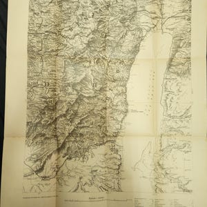 Puede incluir: Una taza de cerámica blanca con un asa negra y el texto "But First, Coffee" en negrita negra. La taza se encuentra sobre un fondo neutro, resaltando su diseño simple.