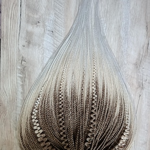 May include: A bundle of synthetic hair extensions featuring a gradient color transition from a dark brown base at the top to a light blonde at the ends. The hair is styled into numerous thin, tight braids with some strands featuring a wavy texture.