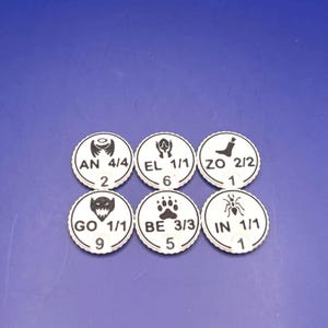 May include: Six white circular game tokens with scalloped edges, each featuring a black icon and text. The tokens display the following labels and values: AN 4/4 with 2, EL 1/1 with 6, ZO 2/2 with 1, GO 1/1 with 9, BE 3/3 with 5, and IN 1/1 with 1.