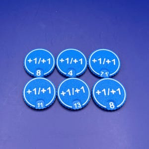 May include: Six circular blue game tokens with a textured surface. Each token features the white printed text +1/+1 and a unique number at the bottom, specifically 8, 4, 71, 11, 13, and 8. The tokens have a ridged edge and a flat design.