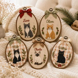 May include: Five oval embroidery hoops featuring stitched cat portraits with names Luna, Oliver, Milo, Charlie, and Willow. Each hoop is decorated with festive greenery, holly, snowflakes, and a satin ribbon bow at the top in various colors.