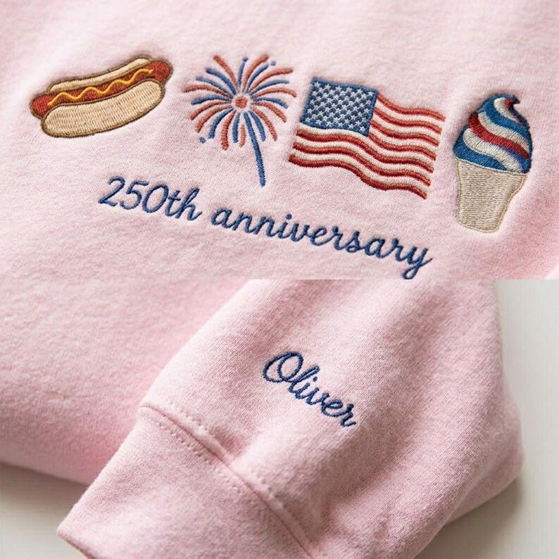 May include: A light pink sweatshirt with embroidered patriotic designs, including a hot dog, fireworks, an American flag, and an ice cream cone. The text "250th anniversary" is embroidered in blue, along with the name "Oliver" on the sleeve.
