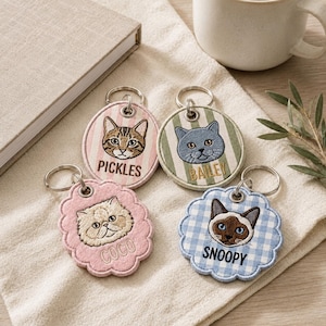 May include: Four circular and scalloped fabric keychains featuring embroidered cat faces and names. Two keychains have striped backgrounds with names Pickles and Bailey, while two have solid or gingham patterns with names Coco and Snoopy.