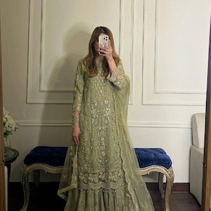 Könnte beinhalten: Ein salbeigrünes formelles Kleid mit aufwendigen Stickereien und Verzierungen. Das Kleid hat lange Ärmel, einen fließenden Rock und einen passenden, durchsichtigen Schal. Der Text "VLUXE FASHION" ist oben zu sehen. Geeignet für besondere Anlässe.