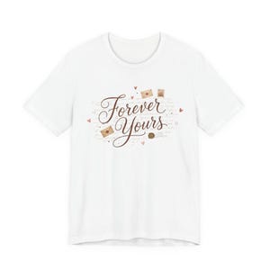 Peut inclure: T-shirt blanc avec l'inscription "Forever Yours" en écriture cursive, ornée de petits cœurs et d'illustrations d'enveloppes. Le motif est centré sur le devant du t-shirt, créant une esthétique romantique et sentimentale.