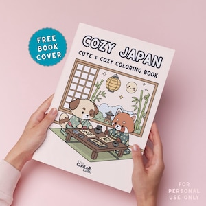 以下が含まれることがあります： 「COZY JAPAN」というタイトルの塗り絵本を人が持っています。「CUTE & COZY COLORING BOOK」というサブタイトルです。表紙には、日本の衣装を着た犬とレッサーパンダのイラストが描かれています。水色のステッカーには「FREE BOOK COVER」と書かれています。