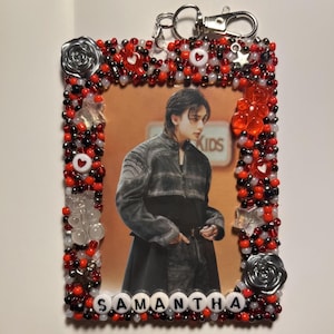 May include: A beaded keychain featuring a photo of a person in a dark jacket. The frame is decorated with red, black, and clear beads, with accents of silver roses, hearts, and stars. The name "SAMANTHA" is spelled out at the bottom.