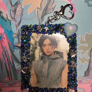 May include: A photo card with a beaded frame featuring a person in a gray vest. The frame is decorated with blue, green, and gold beads, with heart-shaped charms and the word "FAIRIES" at the bottom. A silver heart-shaped clasp is attached.