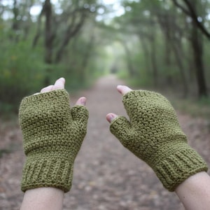 Könnte beinhalten: Ein Paar fingerlose Handschuhe in Olivgrün, gefertigt mit einer strukturierten Häkelmasche. Die Handschuhe verfügen über ein geripptes Bündchen am Handgelenk und eine Daumenöffnung, die Handfläche und Handrücken bedecken und Finger frei lassen.