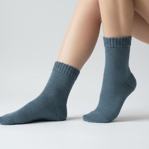 May include: A pair of teal-colored socks. The socks are mid-calf length with ribbed cuffs. The socks are made of a soft, knitted material. The socks are displayed on a person's legs against a white background.