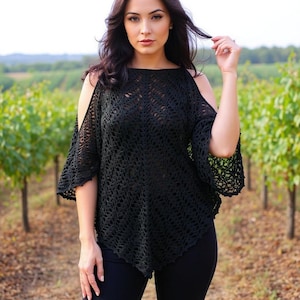 Op de afbeelding: Zwart gehaakt topje met open schouders en uitlopende mouwen. De top heeft een los, vloeiend ontwerp en wordt gecombineerd met een zwarte broek. De afbeelding is buiten gemaakt met een wijngaard op de achtergrond.