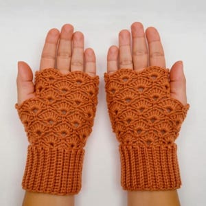 May include: A pair of orange crochet fingerless gloves. The gloves feature a detailed openwork pattern on the hand and a ribbed cuff. The gloves are displayed on a light background.