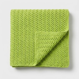 May include: A folded, lime green blanket with a textured, woven pattern. The blanket is square and has a folded corner, revealing the intricate design. The bright green color adds a pop of color to any room.
