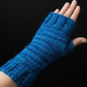 Pode incluir: Uma luva sem dedos de malha azul e verde-azulado. A luva é feita de um fio macio e apresenta um punho canelado e um padrão listrado. A luva foi projetada para manter as mãos aquecidas, deixando os dedos livres.