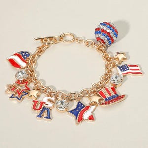 May include: Gold-toned charm bracelet featuring patriotic symbols. Charms include a flag, stars, a hat, and a sphere, all in red, white, and blue. The bracelet has a toggle clasp and is adorned with clear crystal accents.