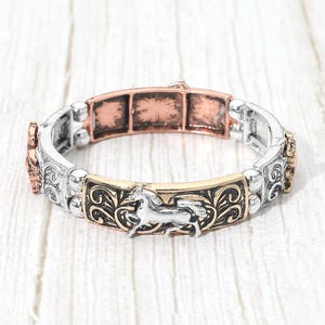 May include: A stretch bracelet featuring alternating rectangular metal links in silver and copper tones. The links display embossed horse figures and intricate scrollwork patterns, connected by small round silver beads in a flexible design.