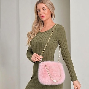 May include: A light pink, fluffy crossbody bag with a gold chain strap and pearl accents. The bag is rectangular with rounded edges. The bag is made of a soft, furry material.