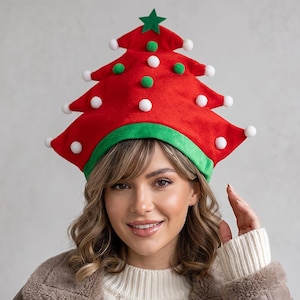 May include: A red felt hat shaped like a Christmas tree with a green brim. The hat features a green star at the top and is decorated with multiple small white and green pom-poms attached to the points and surface of the tree-shaped fabric.