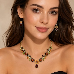 May include: A gold-tone necklace and matching drop earrings set featuring amber-colored teardrop stones, small green enameled leaves, and iridescent floral accents. The necklace has a central flower motif with a dangling teardrop pendant.