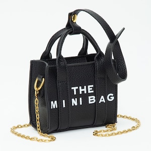 May include: Black mini handbag with gold chain strap and handles. The bag features the text "THE MINI BAG" in white block letters. The bag has a textured surface.