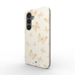 Op de afbeelding: Crèmekleurige telefoonhoes met een herhalend patroon van gouden en bruine aquarel vlinders. De hoes heeft een zwarte cameramodule en een gladde, glanzende afwerking. De vlinders variëren in grootte en zijn verspreid over het oppervlak.