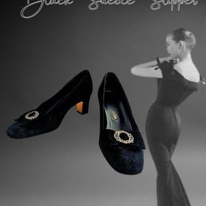 Puede incluir: Zapatos de tacón de ante negro con una hebilla decorativa dorada. Los tacones tienen un pequeño tacón de bloque dorado. El texto "Black Suede Slipper" está en la parte superior de la imagen.