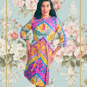 May include: A colorful, patterned dress with a zip-up front and a matching belt. The dress features a vibrant mix of pink, yellow, blue, and purple geometric designs. The sleeves are three-quarter length, and the dress is knee-length.
