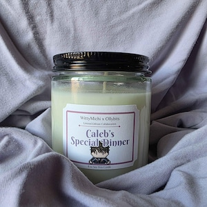 Può includere: Una candela in barattolo di vetro con coperchio nero, etichettata "Caleb's Special Dinner". L'etichetta presenta pixel art e il testo "WittyMichi x Ollybits". La candela è da 227g ed è fatta di cera di soia.
